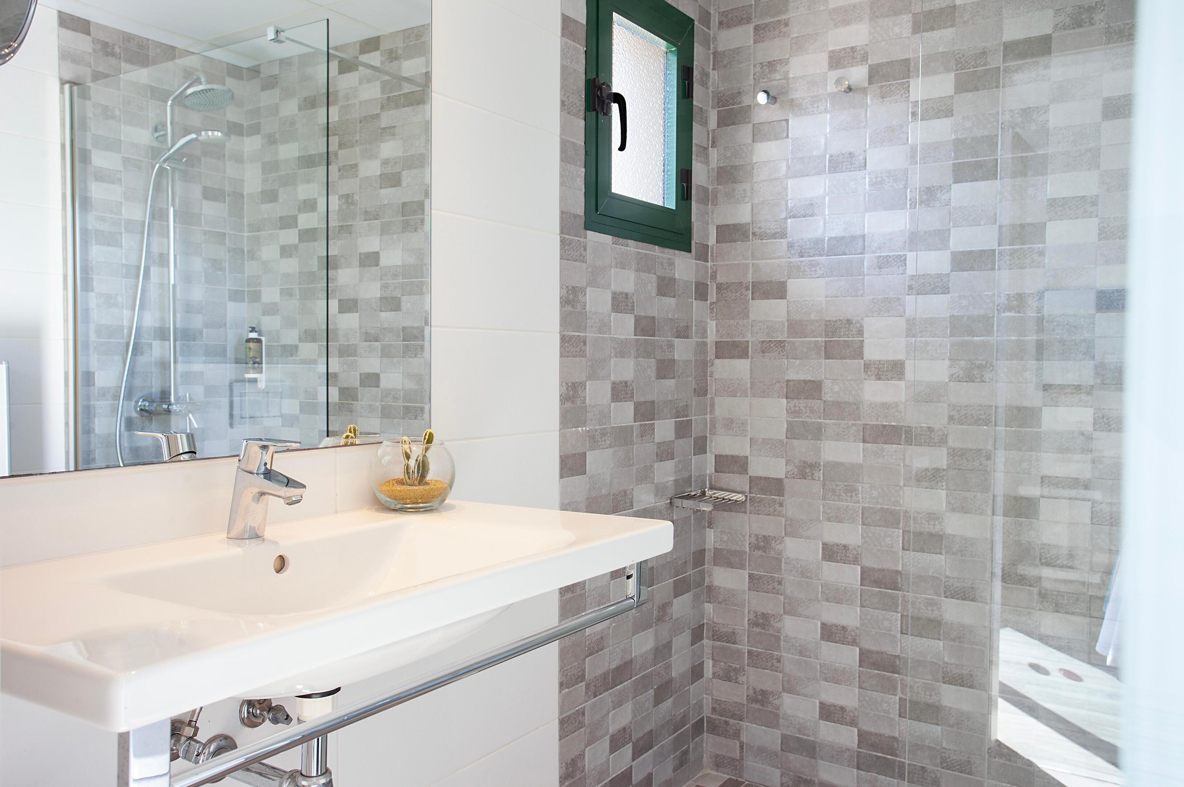 Un baño moderno con un lavamanos grande, mampara de vidrio para la ducha y pared con azulejos.