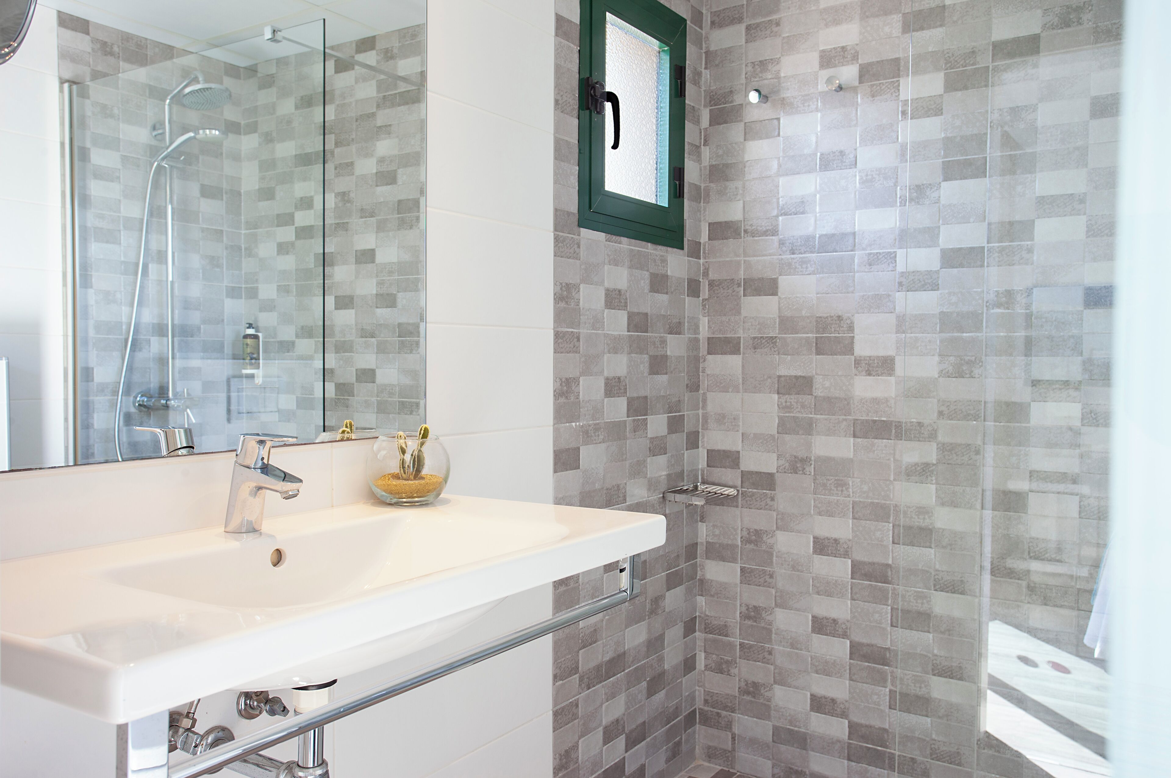 Un baño moderno con cabina de ducha de vidrio, un lavabo blanco y pared de ducha azulejada.