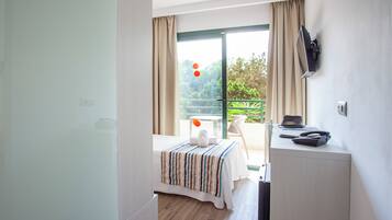 Habitación de hotel con cama, escritorio, silla y balcón con vistas a la vegetación.