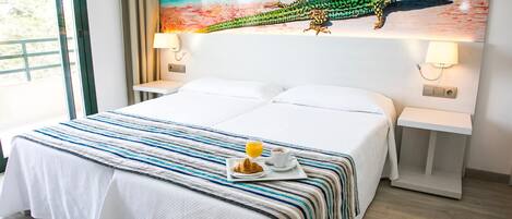 Habitación de hotel con una cama grande, una bandeja de desayuno con cruasanes y jugo de naranja, y un cuadro de un lagarto en la pared.