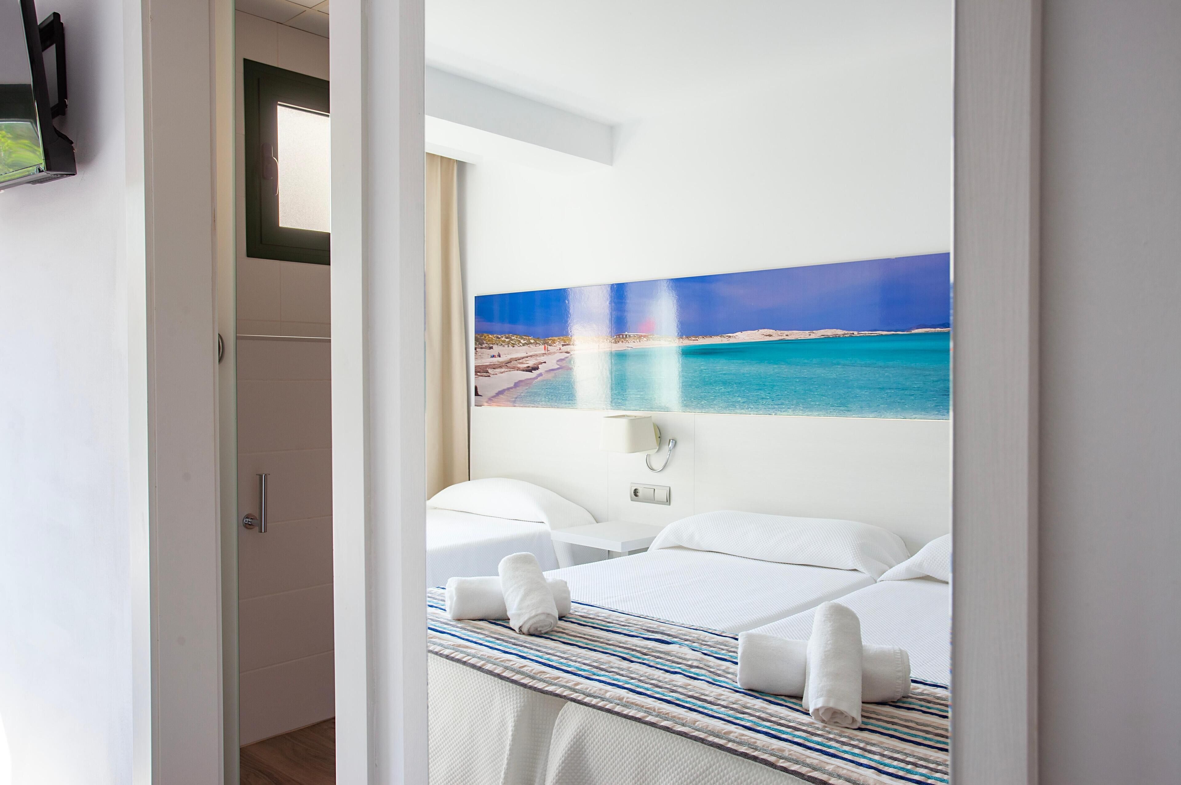 Een hotelkamer met een bed, nachtkastje en een schilderij van een strand.
