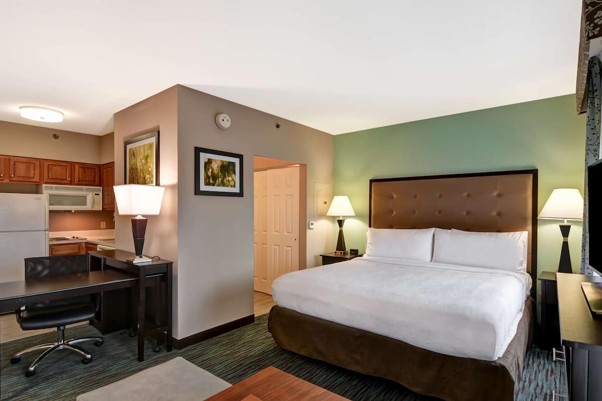 Ein Hotelzimmer mit Bett, Schreibtisch, Stuhl und Küchenzeile.