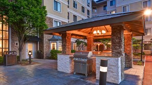 Un espace extérieur aménagé en patio, avec un coin barbecue, des piliers en pierre et un espace salon abrité.