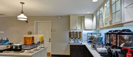 A modern kitchen with a breakfast bar, coffee machines, and a juice dispenser.