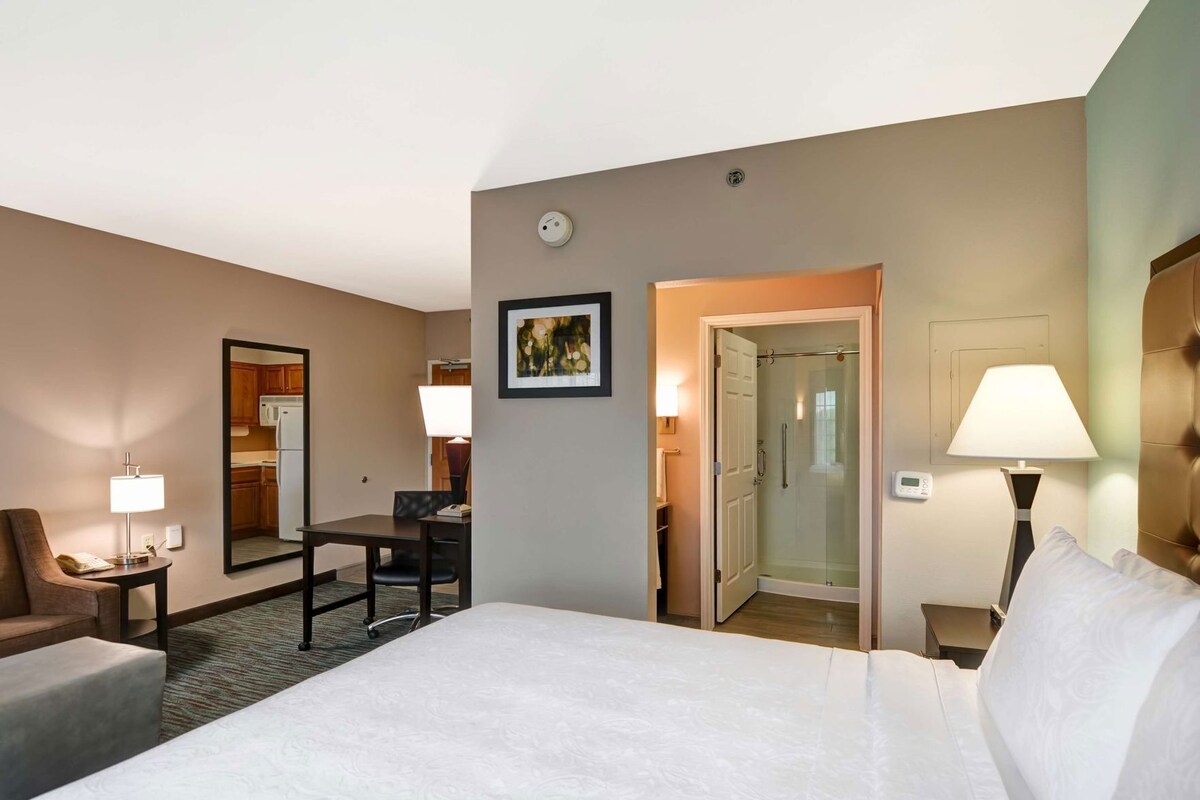 Een hotelkamer met een bed, een bureau, een stoel, een bank, een lamp en een deur naar een badkamer.