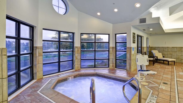 Un espace piscine intérieur moderne, doté de grandes fenêtres, d’un jacuzzi central et de chaises longues.