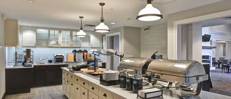 A modern kitchen with a central island, overhead pendant lights, and a built-in grill.