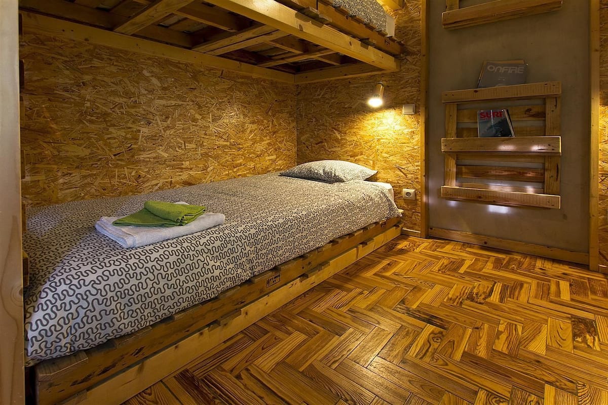 Una habitación acogedora con una cama nido de madera, una colcha estampada y un pequeño estante con revistas.