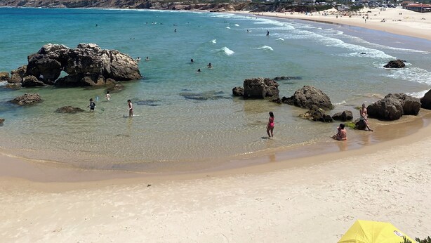 A beach with clear water, rocks, and people. - Eco Hostel - Tribo da Praia (Peniche)