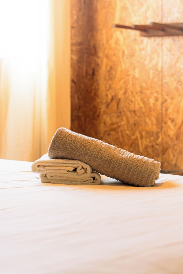 Une serviette beige, soigneusement pliée, est posée sur un lit dont la tête de lit est en bois.