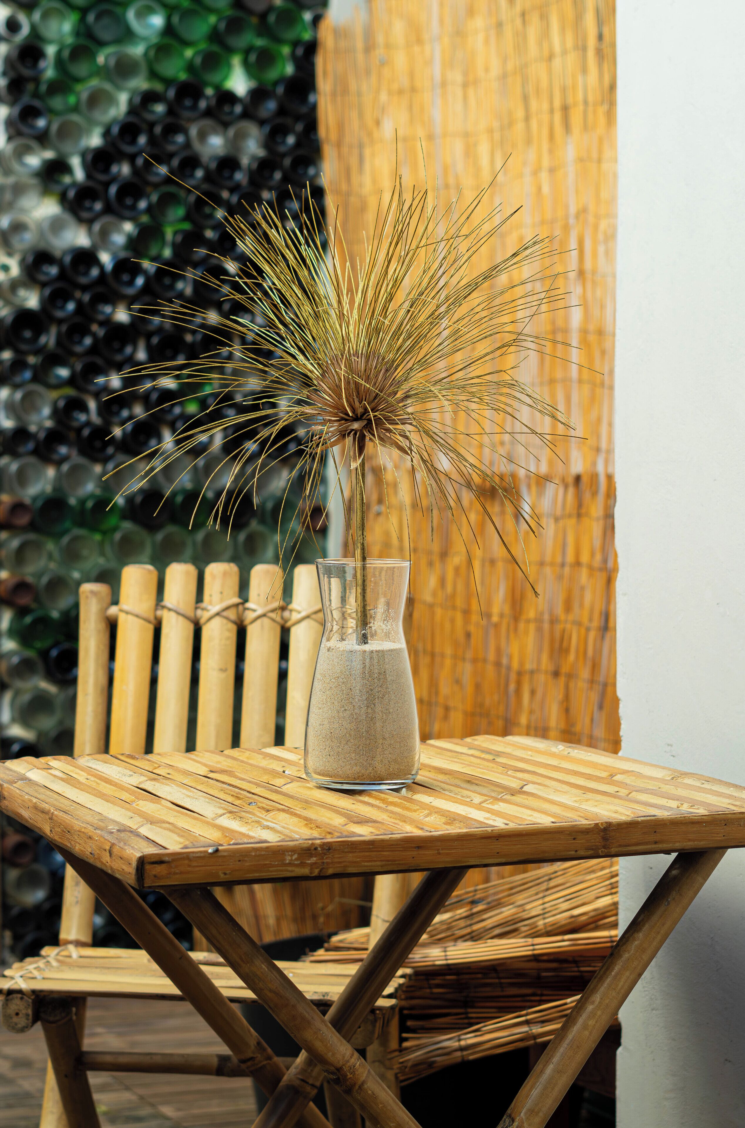 A bamboo table with a glass vase containing a dried plant.