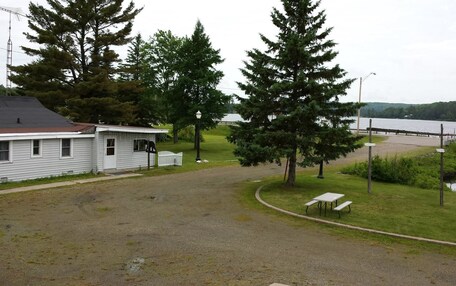 A small cabin with a gravel driveway, a picnic table, and a bench near a lake.