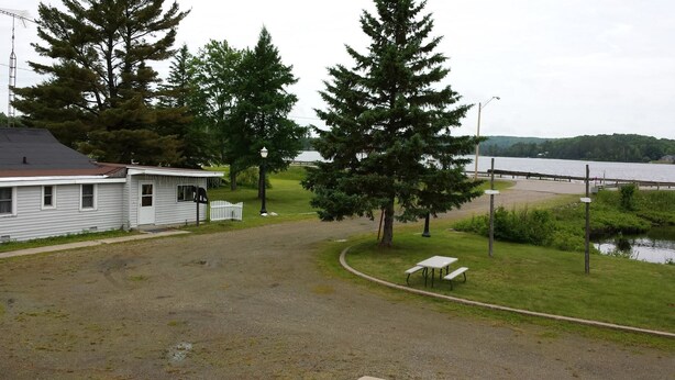 A small cabin with a gravel driveway, a picnic table, and a bench near a lake. - Bear Paw Inn (Michigamme)