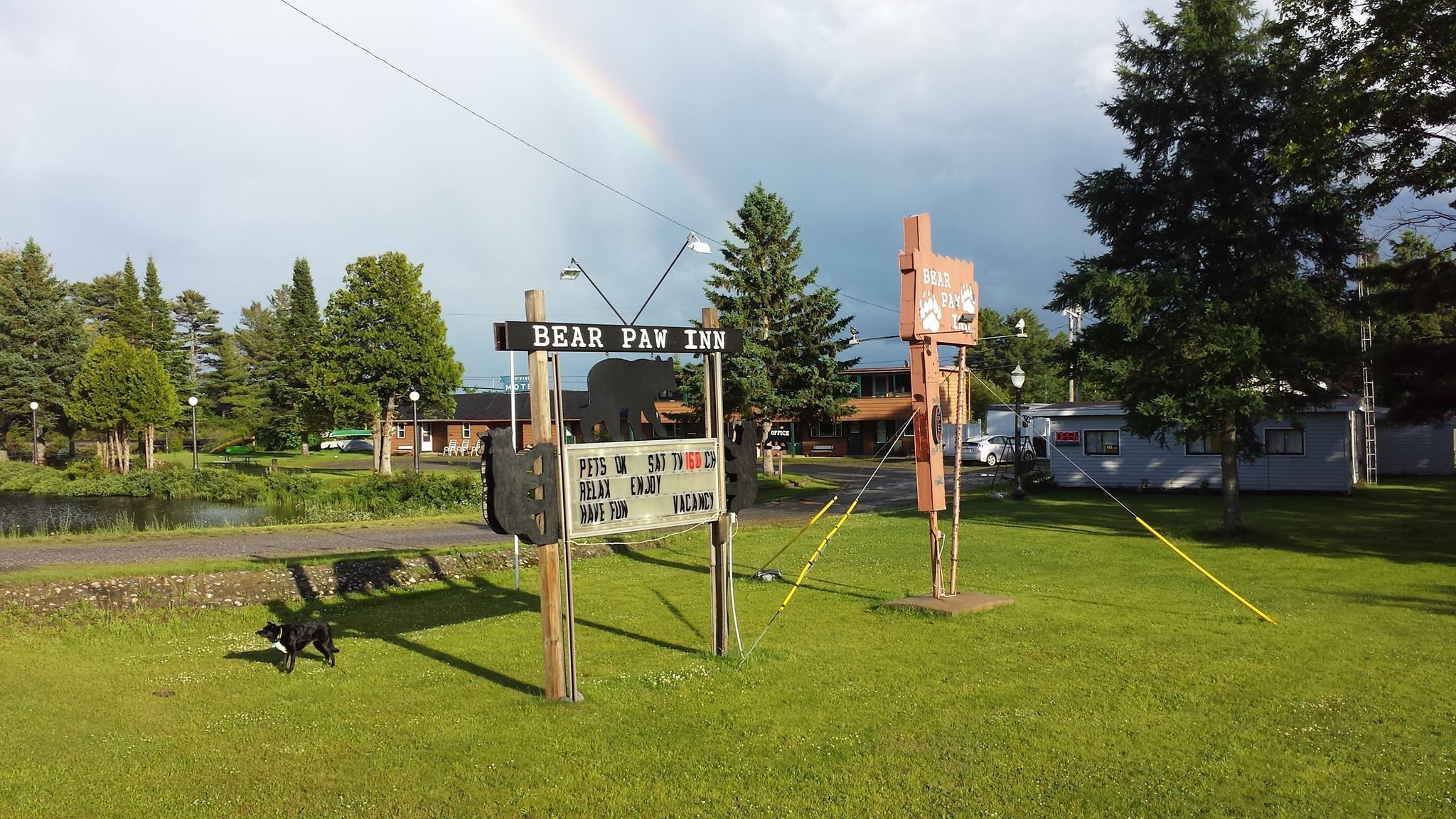 A sign for Bear Paw Inn with a bear silhouette, a sign for a pet-friendly establishment, and a rainbow in the background.