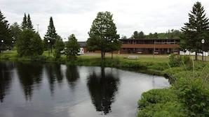 A tranquil lakeside setting with a building featuring a red facade and multiple windows, surrounded by lush greenery and trees. - Bear Paw Inn (Michigamme)