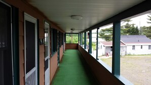 A long corridor with green carpeting, large windows, and a view of a residential area. - Bear Paw Inn (Michigamme)