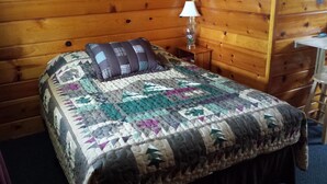 A wooden cabin room with a bed, a nightstand, and a lamp. - Bear Paw Inn (Michigamme)
