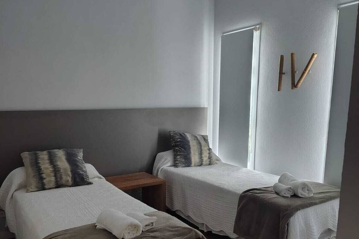 A twin bedroom with two beds, a nightstand, a window, and a door with a handle.