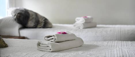 Una cama bien hecha con toallas dobladas y un edredón enrollado, una almohada y un gato sentado en la cama.