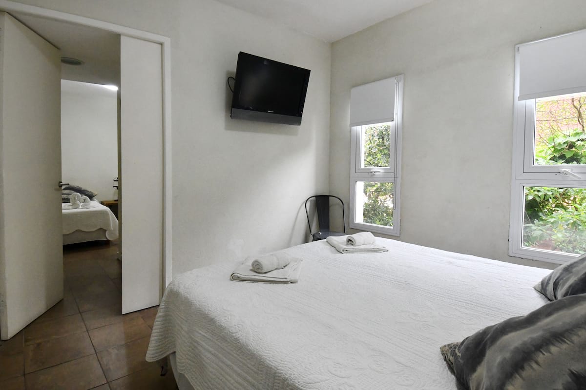 A bedroom with a bed, a TV mounted on the wall, and a window with a view of greenery.