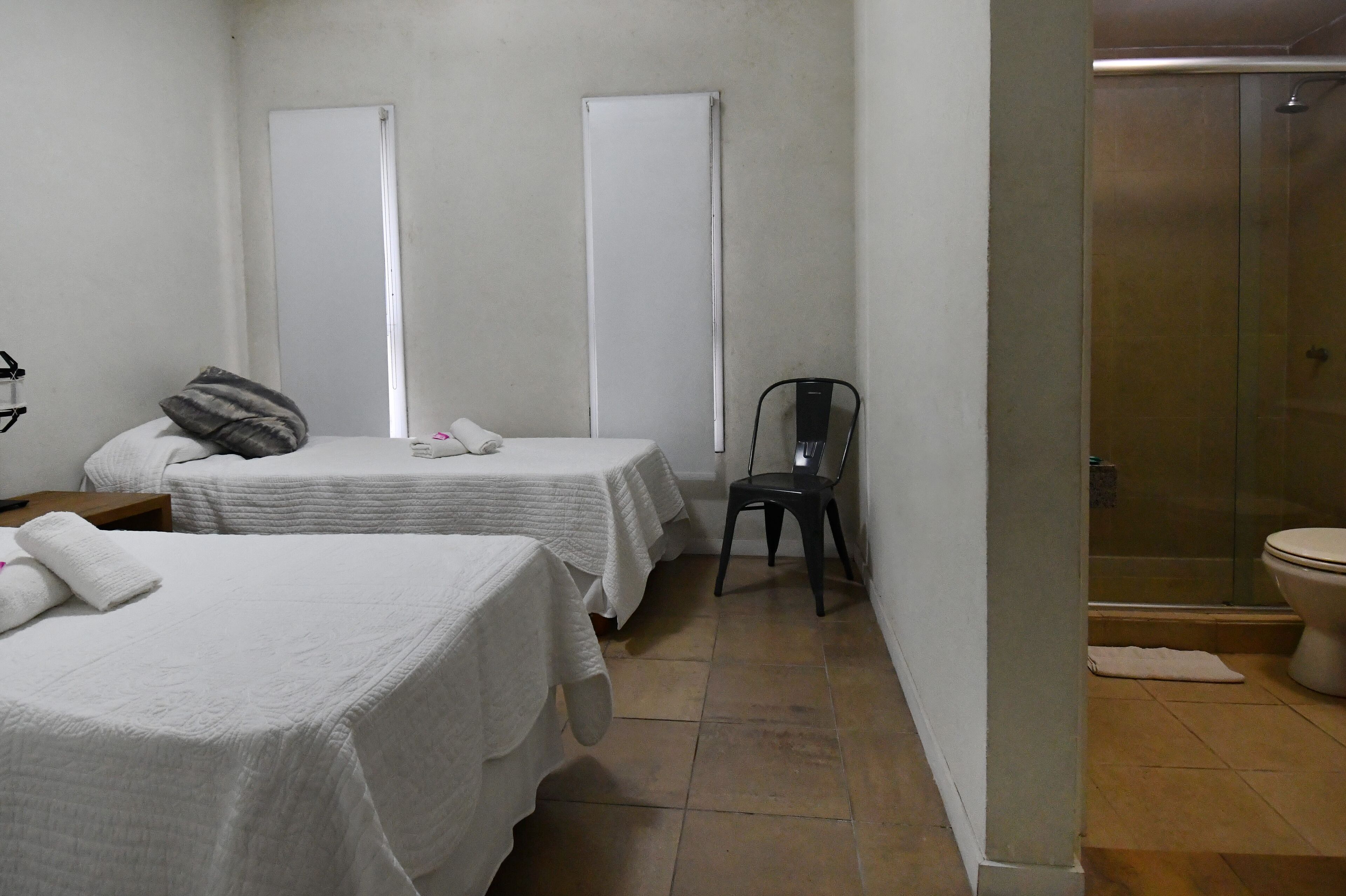 A hotel room with two beds, a chair, a shower, and a toilet.