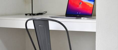 Un escritorio blanco con una computadora portátil, una silla gris y una lámpara de escritorio negra.