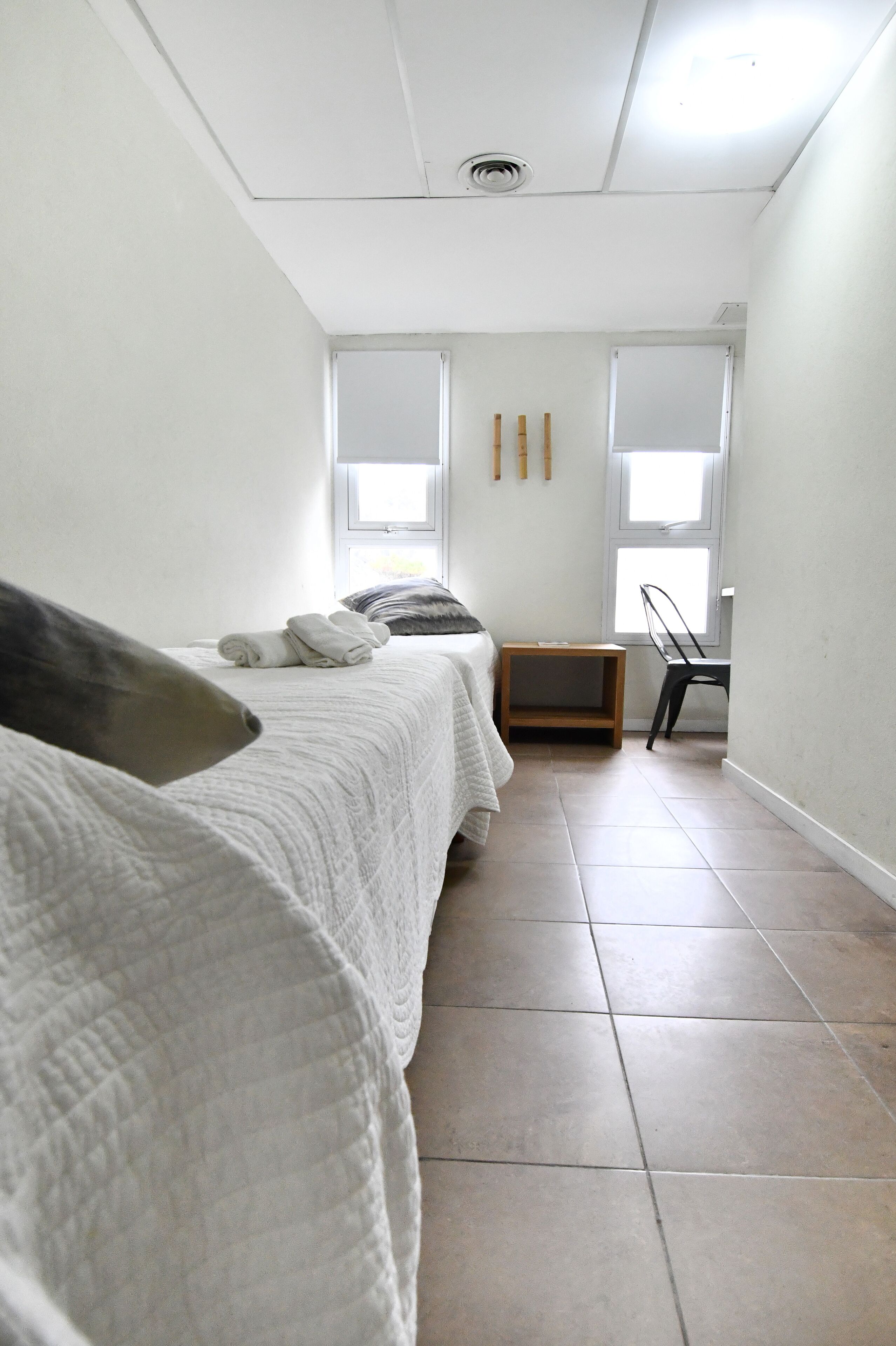 A bedroom with a bed, a small wooden nightstand, a chair, and two windows.