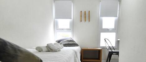 A bedroom with a bed, a small wooden nightstand, a chair, and two windows.