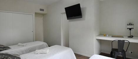 A room with two beds, a desk, a chair, a television, and a door.