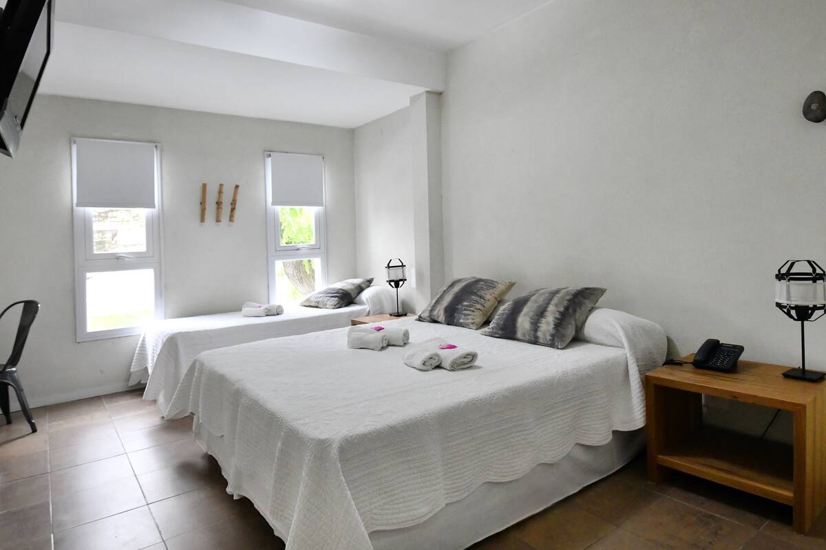 A hotel room with two beds, a wooden nightstand, a telephone, and a window with blinds.