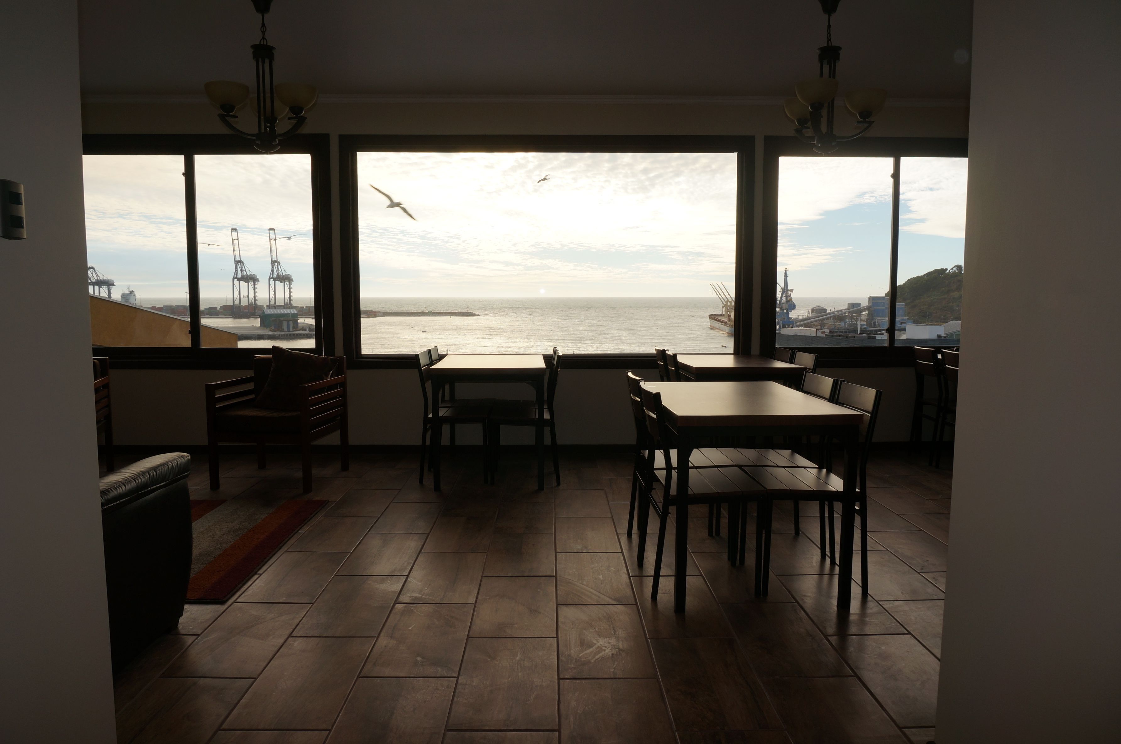 Una habitación con un amplio ventanal que da a un puerto, con zona de comedor, sillas y mesa.