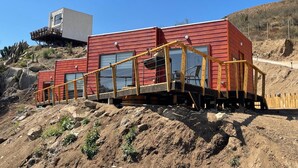 Un edificio moderno rojo con una terraza de madera y una estructura pequeña adosada.