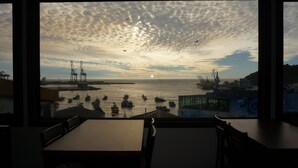 Vista desde un restaurante con un ventanal grande que da a un puerto al atardecer.