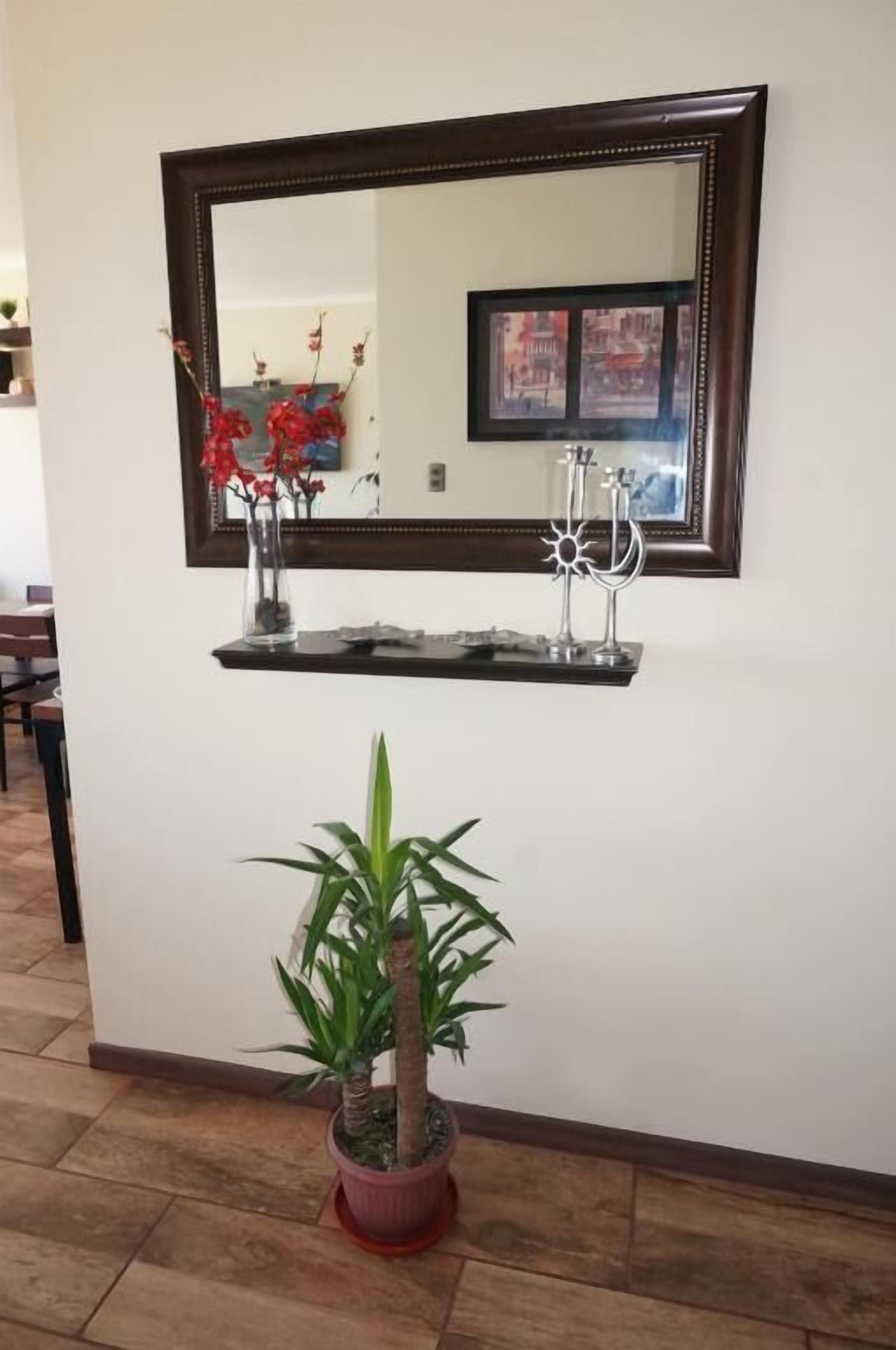 A mirror with a decorative frame, a small shelf with a candle holder, and a potted plant.
