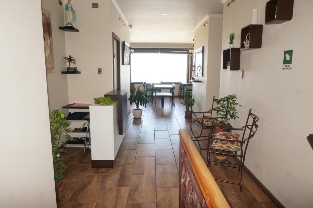 A hotel corridor with a dining area at the end, potted plants, and a statue on the wall.
