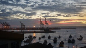 Un puerto al atardecer con grúas y barcos.