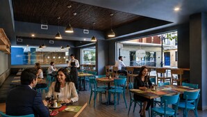 A restaurant interior with wooden tables, teal chairs, and hanging pendant lights. - Novapark (Santiago)