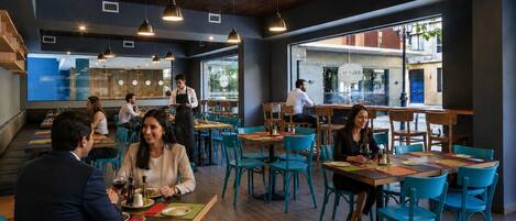 A restaurant interior with wooden tables, teal chairs, and hanging pendant lights.