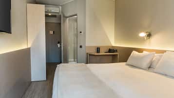 Una habitación de hotel con cama, mesita de noche, televisor de pared y puerta que da al baño.