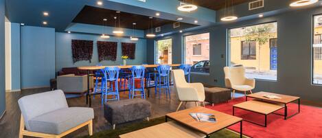 Un salón moderno con paredes azules, techo de madera y alfombra roja. Incluye zonas de estar con sillas azules y blancas, un sofá y una mesa de centro.