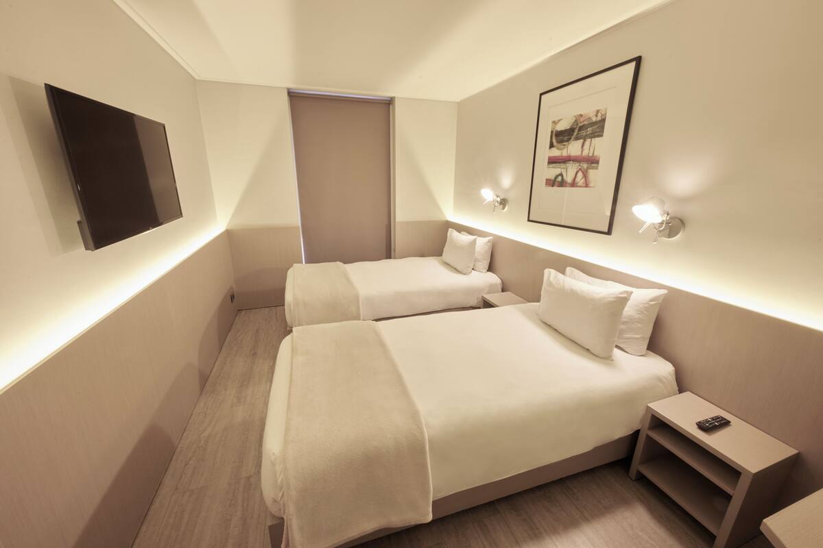 Una habitación de hotel con dos camas, un televisor de pantalla plana, un cuadro enmarcado y una mesita de noche con un control remoto.