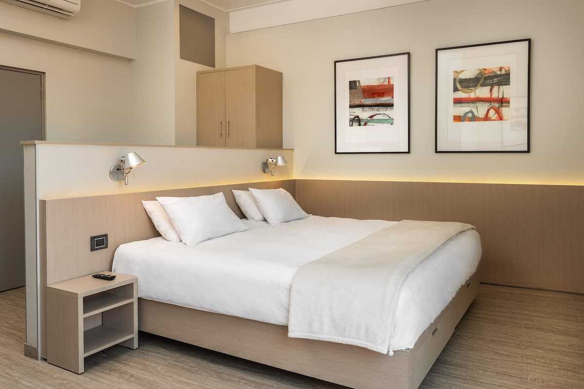 Una habitación de hotel moderna con una cama grande, mesitas de noche y obras de arte en las paredes.