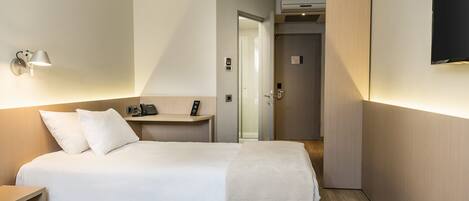 A hotel room with two beds, a desk with a phone, a wall-mounted TV, and a door leading to a bathroom.
