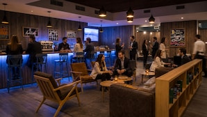 A bar area with stools, a counter, and a seating area with a sofa and tables. - Novapark (Santiago)