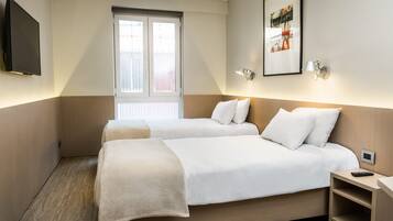 Habitació d'hotel amb dos llits, televisió penjada a la paret, finestra amb persianes i un quadre encimbellat a la paret.