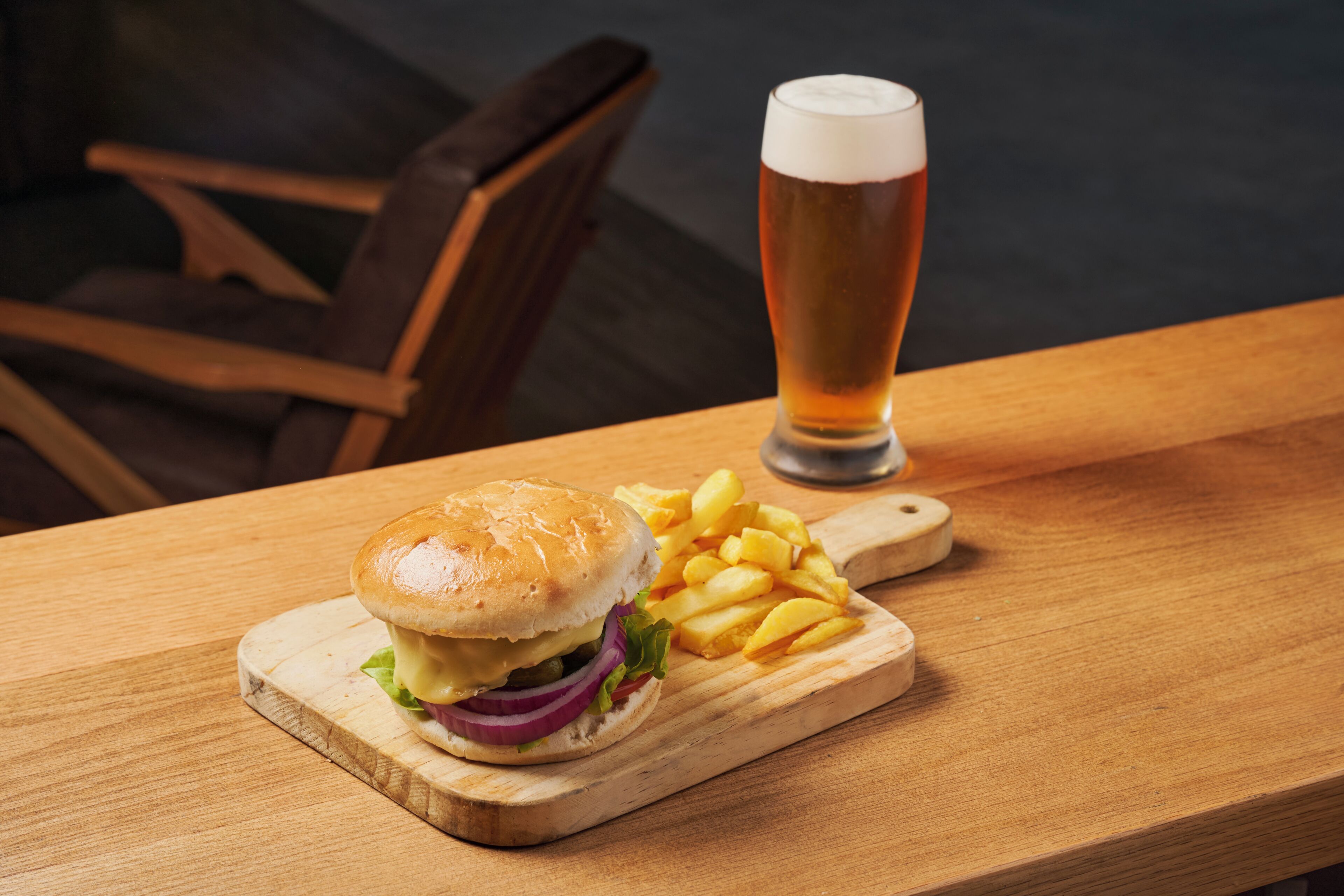 A wooden table with a burger, fries, and a glass of beer.
