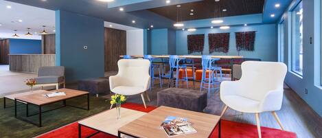 Un área de lounge moderna con mesas de madera, sillas blancas y alfombra roja.