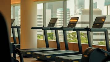 Un gimnasio con cintas de correr y equipo de ejercicio, ventanas amplias y vistas a edificios de la ciudad.