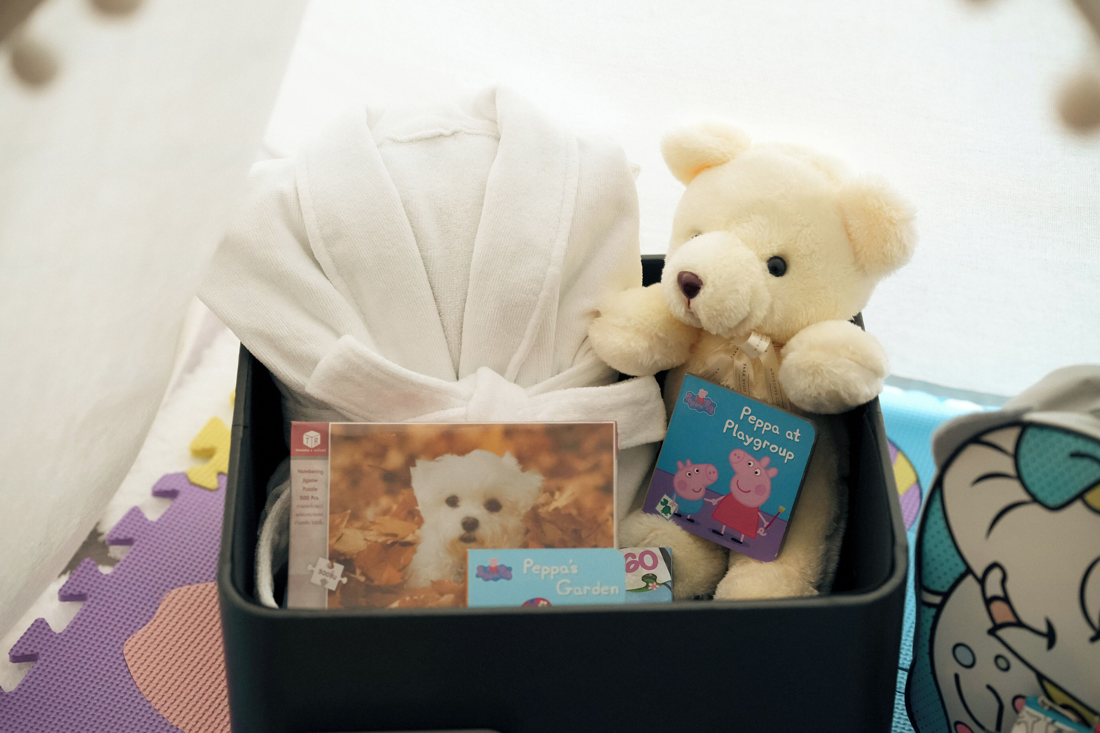 A storage bin containing a white teddy bear, Peppa Pig-themed books, and a Peppa Pig card.