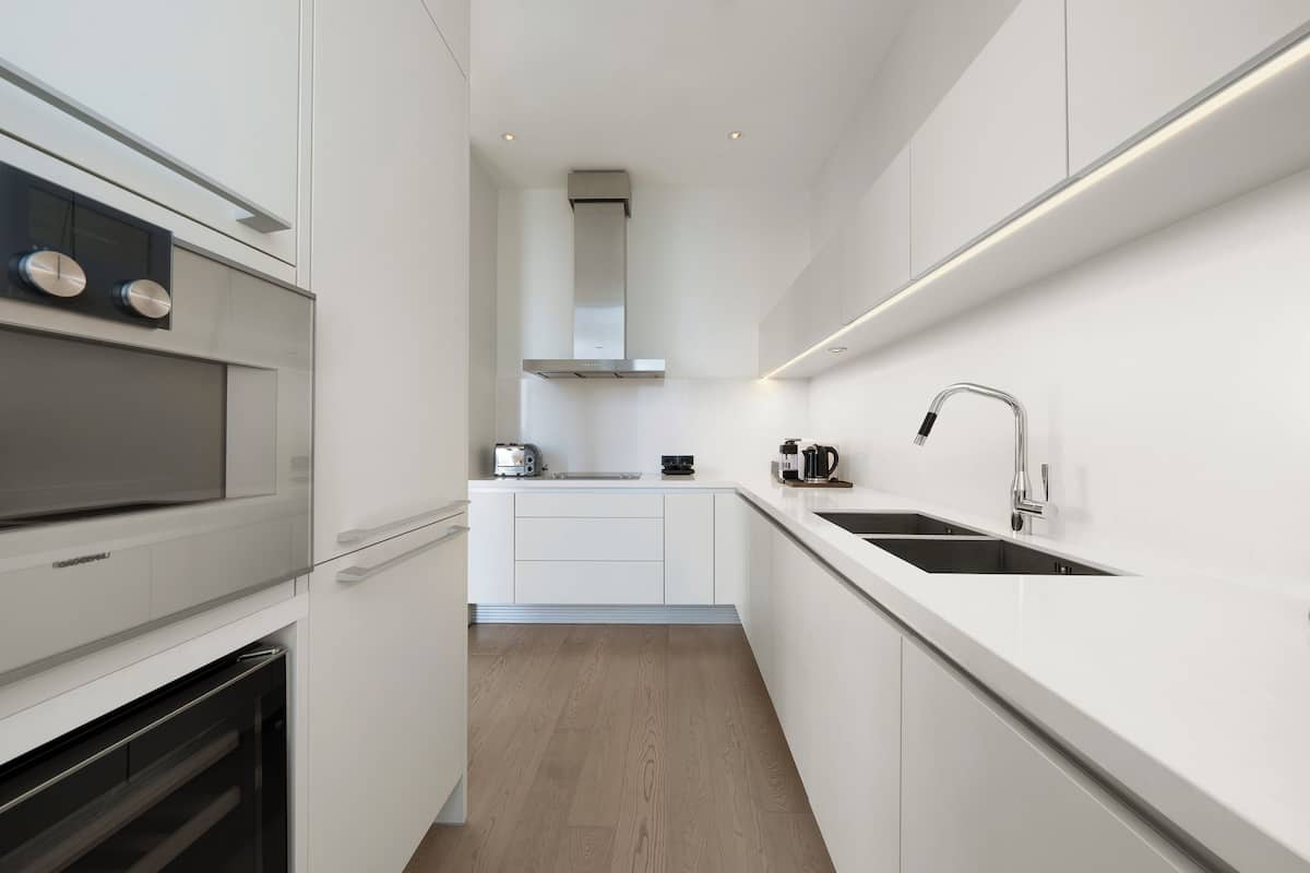 Une cuisine moderne avec des meubles blancs, des appareils en acier inoxydable et un plancher en bois.